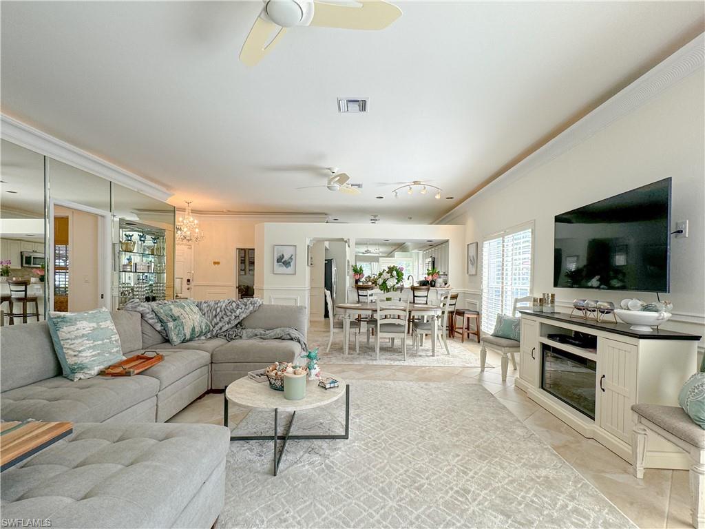 Tiled living room with ceiling fan with notable chandelier and crown molding