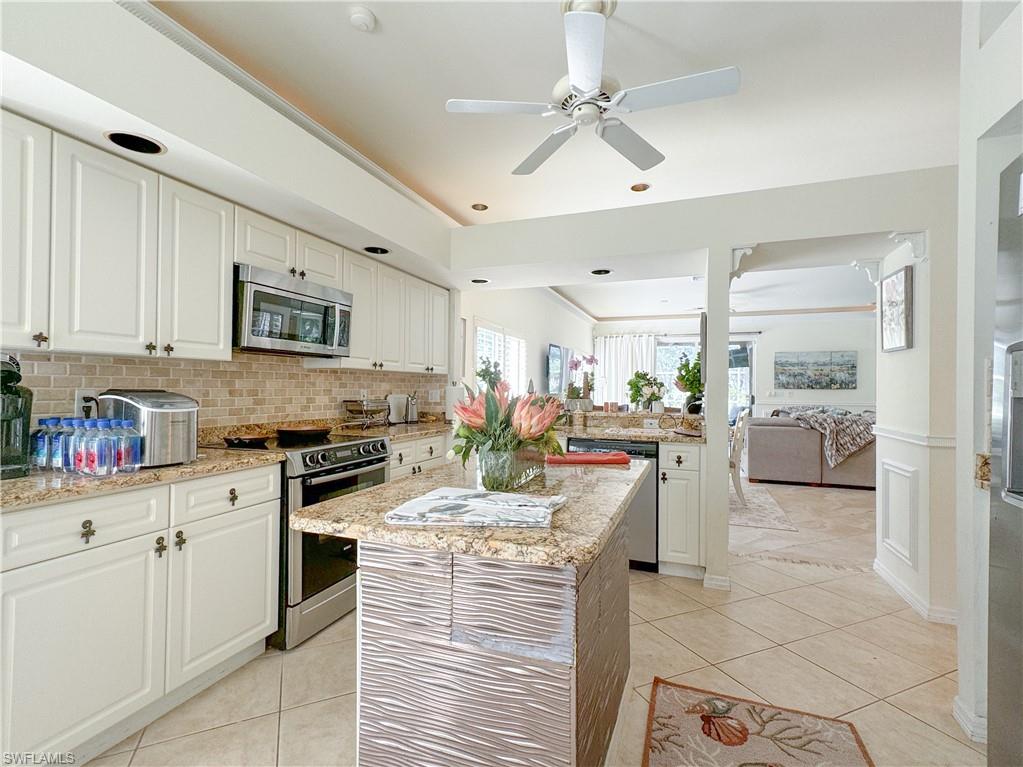 Kitchen with stainless steel appliances, backsplash, white cabinetry, a center island, and light stone countertops