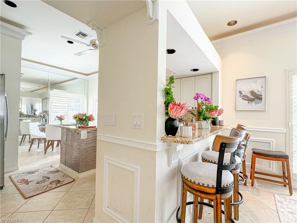 Kitchen featuring light tile floors, light stone counters, ceiling fan, and a breakfast bar