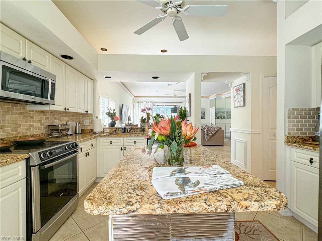 Kitchen with stainless steel appliances, white cabinets, light stone counters, backsplash, and ceiling fan
