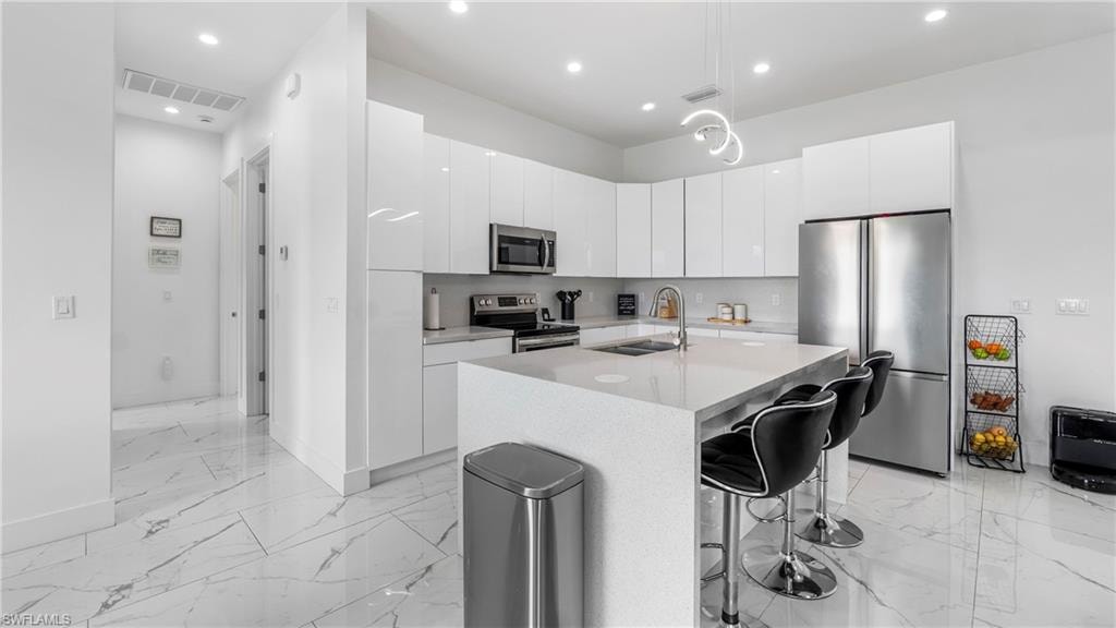 Kitchen featuring stainless steel appliances, modern cabinets, a center island with sink, and white cabinetry