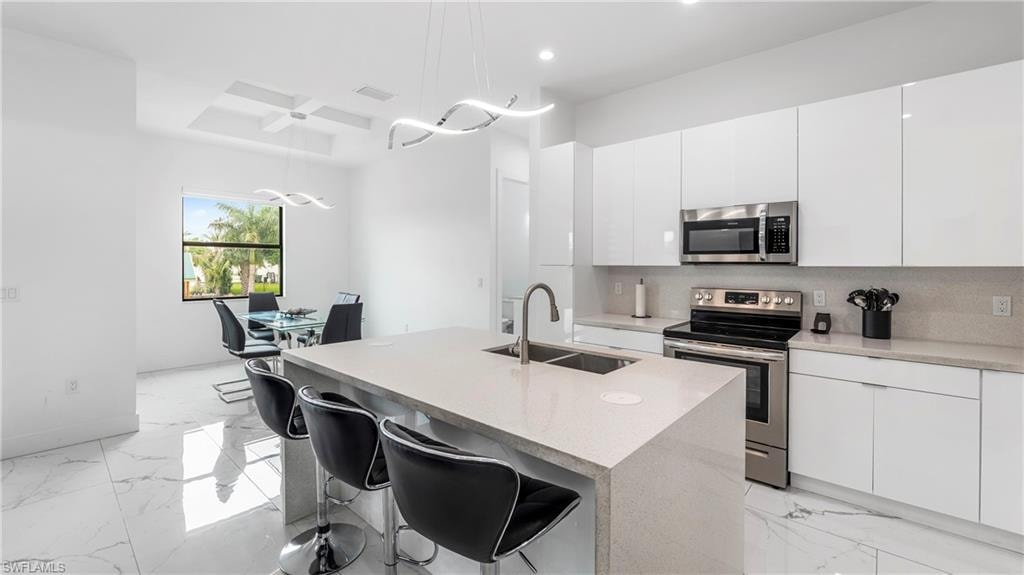 Kitchen featuring stainless steel appliances, a kitchen bar, white cabinets, and modern cabinets