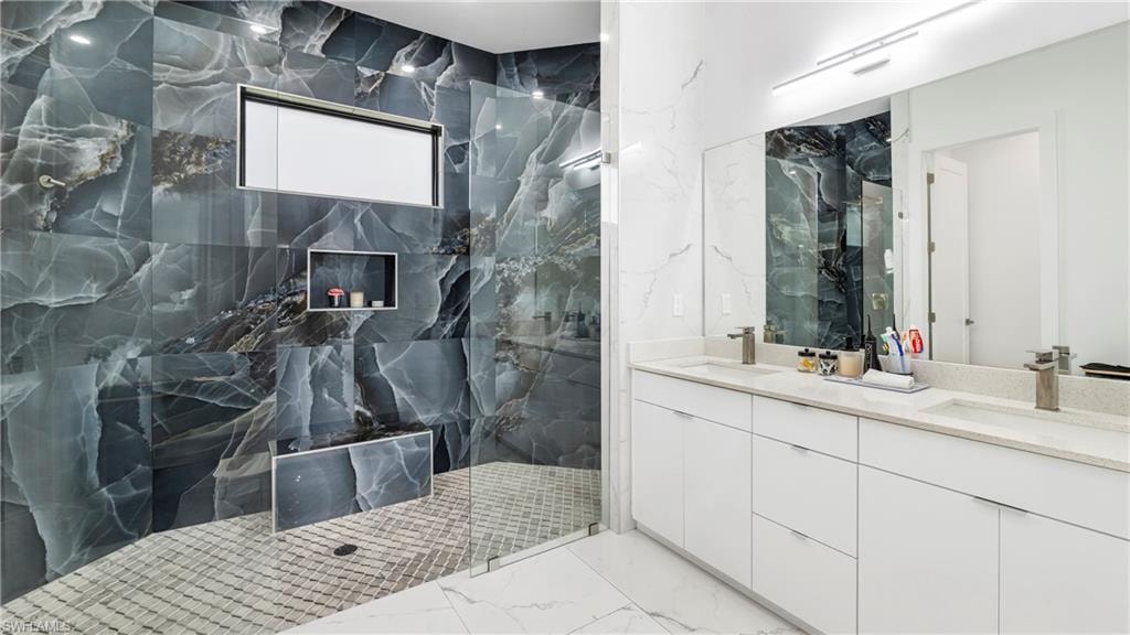 Bathroom featuring double vanity, a marble finish shower, stone wall, and light marble finish flooring