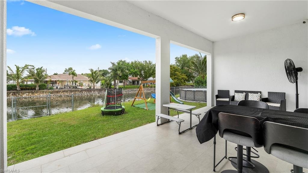 Fenced backyard with a patio, outdoor dining space, a playground, a trampoline, and a water view