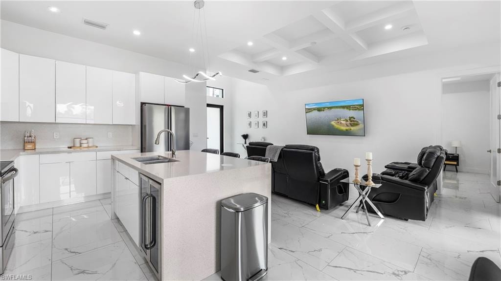 Kitchen with open floor plan, coffered ceiling, an island with sink, beverage cooler, and stainless steel appliances