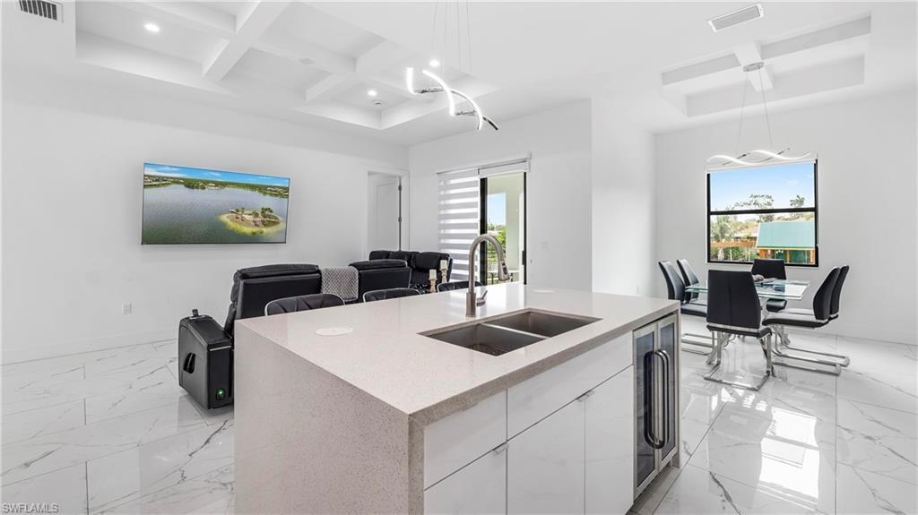 Kitchen featuring coffered ceiling, a kitchen island with sink, open floor plan, light stone countertops, and plenty of natural light