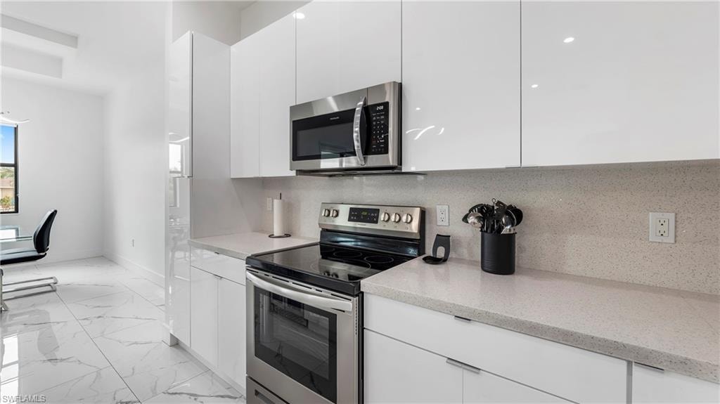 Kitchen featuring stainless steel appliances, white cabinets, modern cabinets, and light marble finish floors