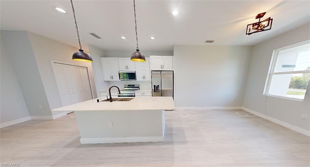 Kitchen with white cabinets, an island with sink, decorative light fixtures, stainless steel appliances, and light wood-style flooring