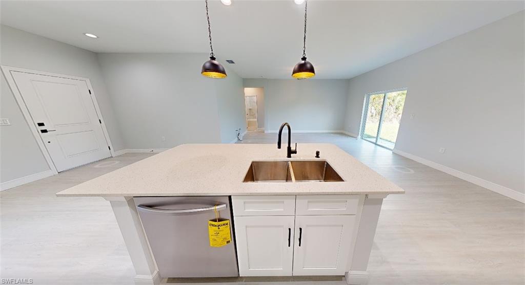 Kitchen with dishwasher, light wood-style flooring, white cabinetry, pendant lighting, and a kitchen island with sink