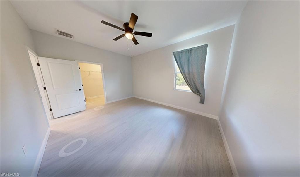 Unfurnished bedroom with a walk in closet, light wood-style floors, and a ceiling fan