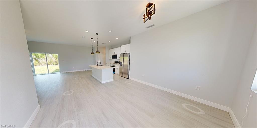 Kitchen featuring open floor plan, white cabinetry, an island with sink, stainless steel appliances, and light wood-style floors