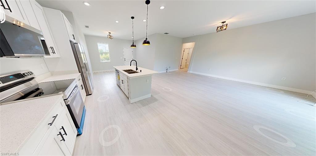 Kitchen with white cabinetry, stainless steel appliances, a kitchen island with sink, open floor plan, and decorative light fixtures