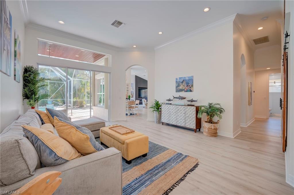 Living room with arched walkways, light wood-style flooring, crown molding, and recessed lighting