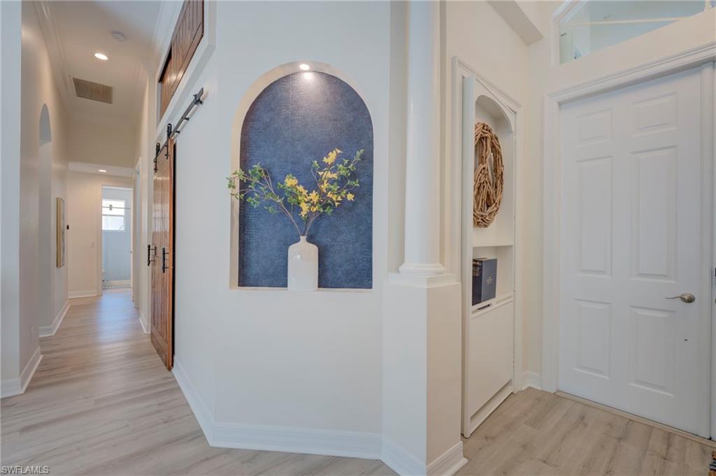 Hall featuring a barn door, light wood-style flooring, arched walkways, and recessed lighting