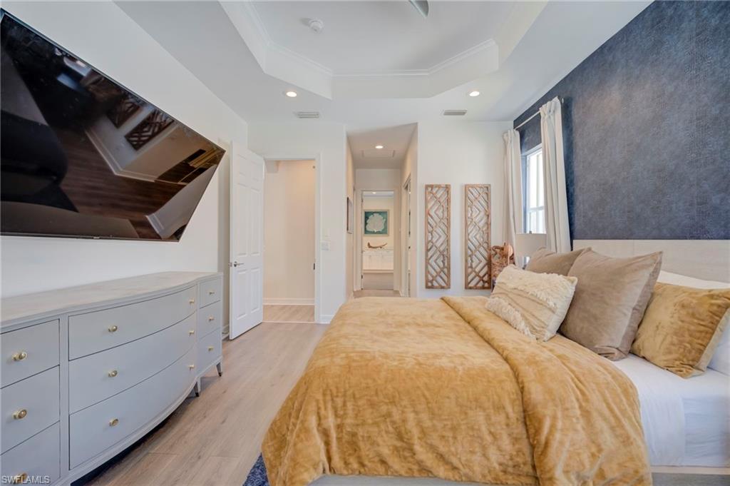 Bedroom featuring light wood-style flooring, connected bathroom, a raised ceiling, recessed lighting, and crown molding