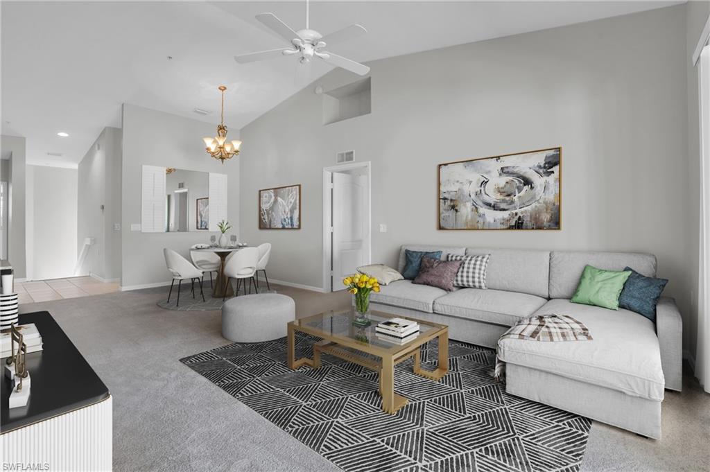Living room with ceiling fan with notable chandelier, carpet floors, and high vaulted ceiling
