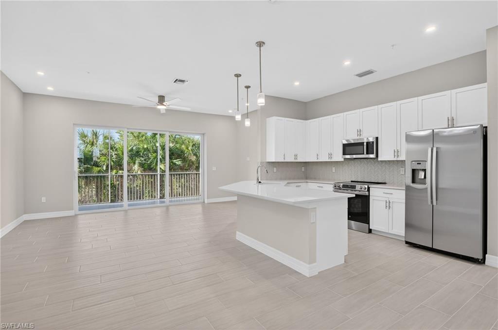 Kitchen with stainless steel appliances, light countertops, pendant lighting, and white cabinets
