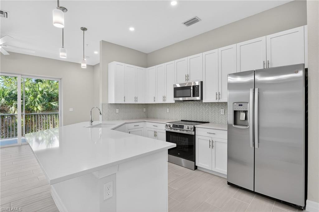 Kitchen with stainless steel appliances, a peninsula, decorative light fixtures, white cabinetry, and decorative backsplash
