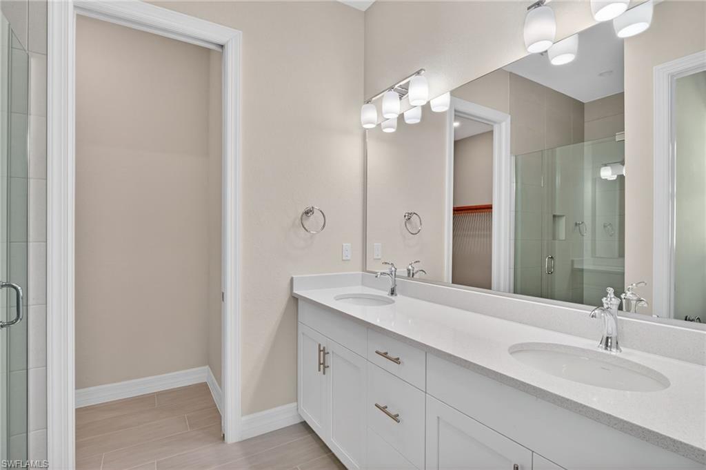 Bathroom with a stall shower, double vanity, a spacious closet, and wood finish floors