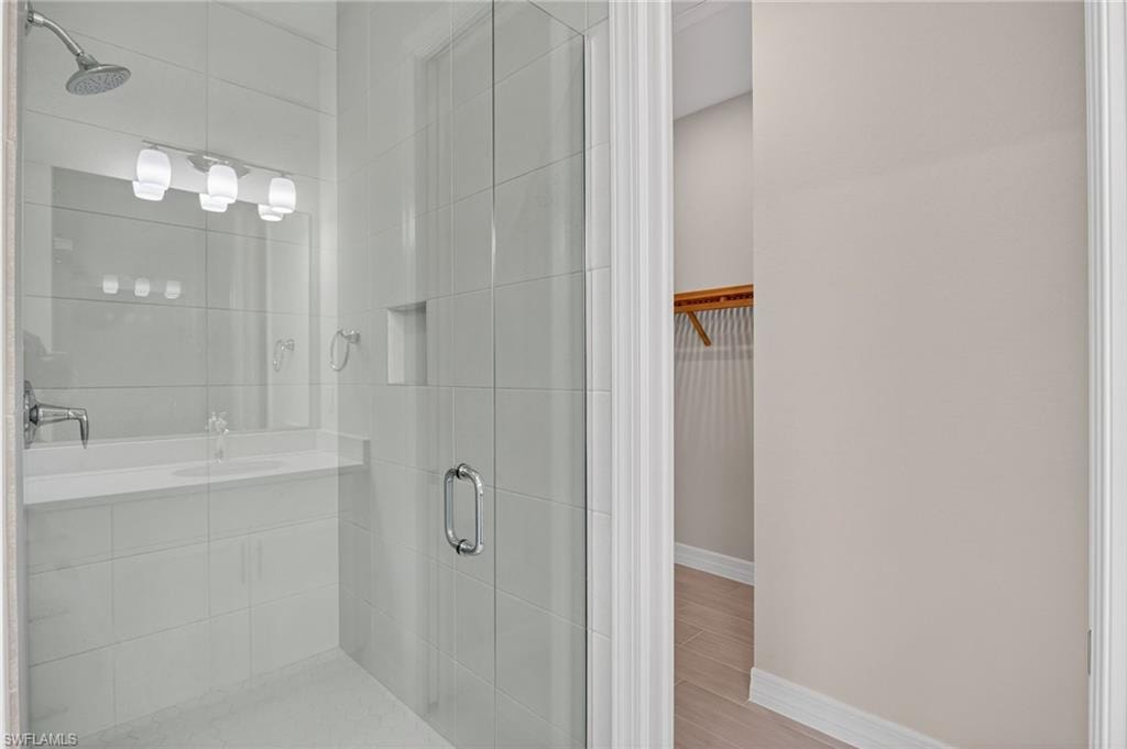 Bathroom featuring a walk in closet, vanity, a shower stall, and light wood finished floors