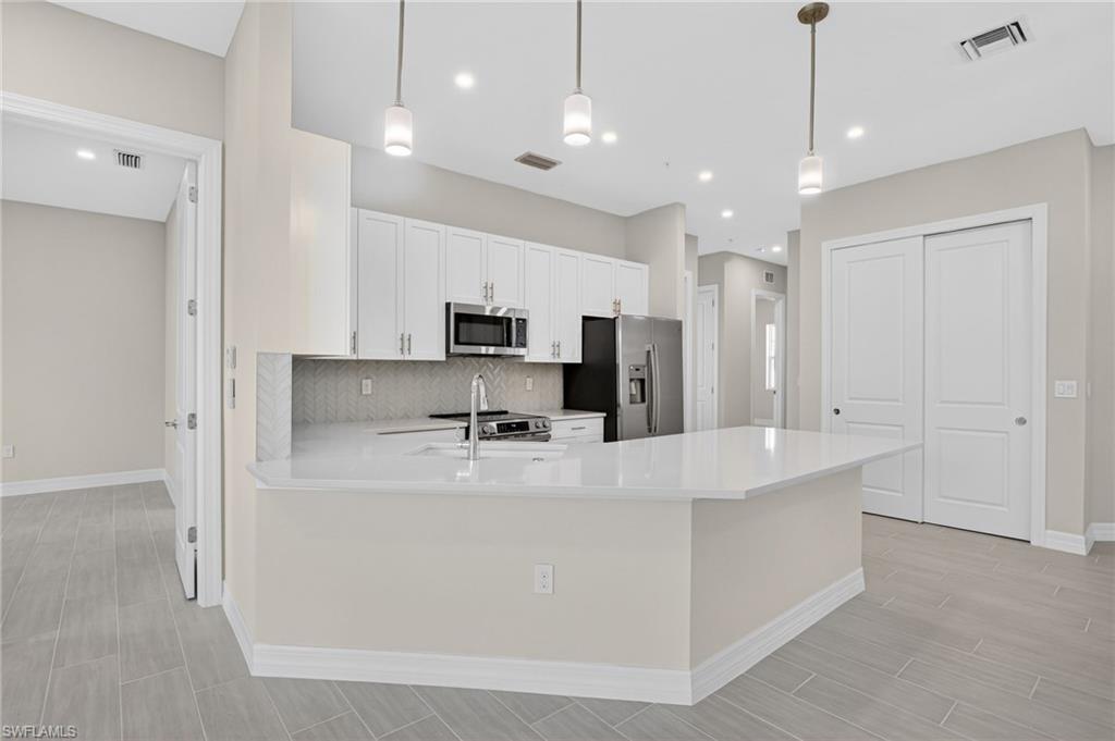 Kitchen with a peninsula, white cabinets, stainless steel appliances, and hanging light fixtures