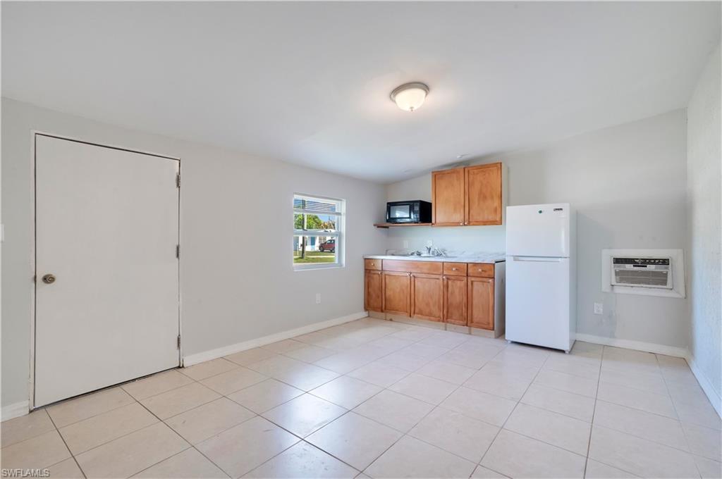 Kitchen featuring light countertops, freestanding refrigerator, wood finish cabinets, black microwave, and light tile patterned floors