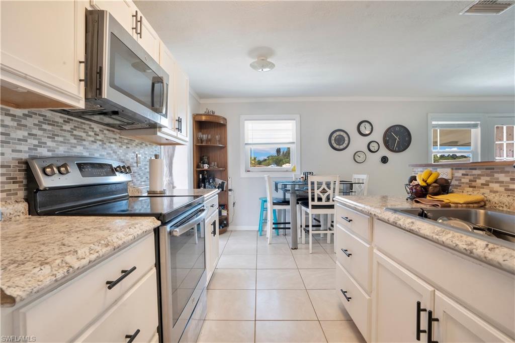 Kitchen featuring backsplash, stainless steel appliances, white cabinetry, light tile patterned floors, and ornamental molding