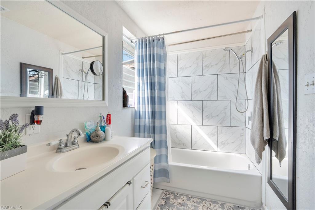 Bathroom featuring vanity, shower / tub combo with curtain, and a textured wall