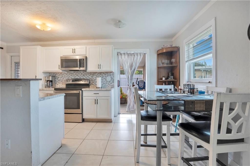 Kitchen featuring stainless steel appliances, white cabinetry, tasteful backsplash, light tile patterned floors, and light stone countertops