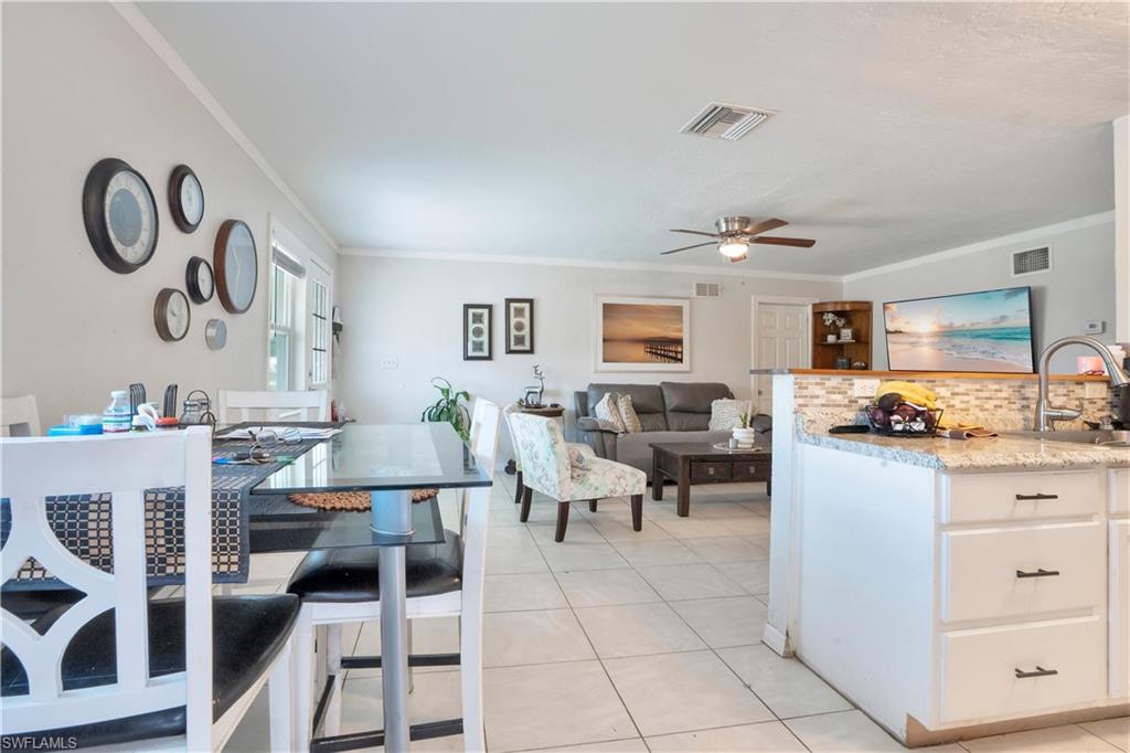 Kitchen featuring white cabinets, ornamental molding, a ceiling fan, light stone counters, and light tile patterned flooring