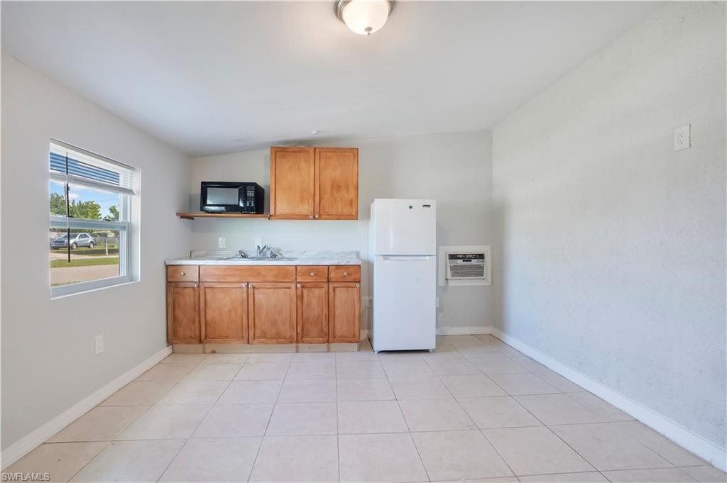 Kitchen featuring wood finish cabinets, light countertops, freestanding refrigerator, black microwave, and light tile patterned floors