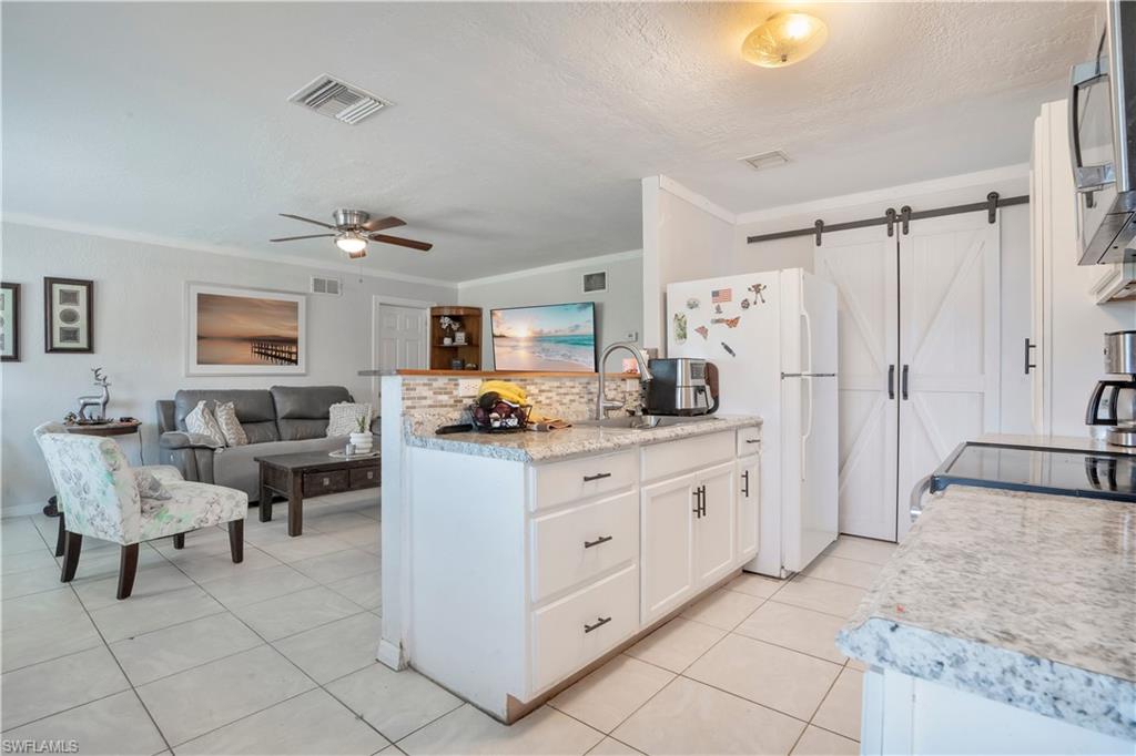 Kitchen with a barn door, white cabinetry, light countertops, a peninsula, and a ceiling fan