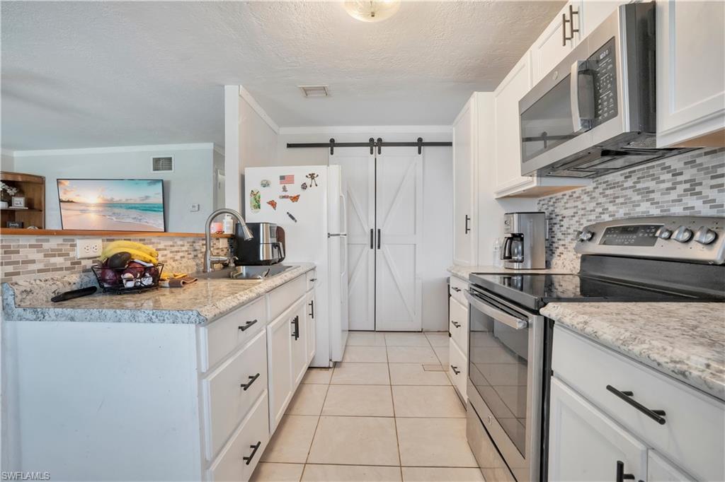Kitchen with backsplash, stainless steel appliances, a barn door, white cabinetry, and crown molding