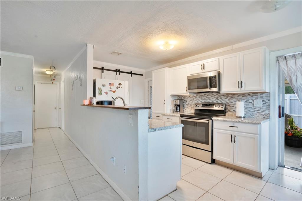 Kitchen with a barn door, stainless steel appliances, white cabinets, backsplash, and ornamental molding