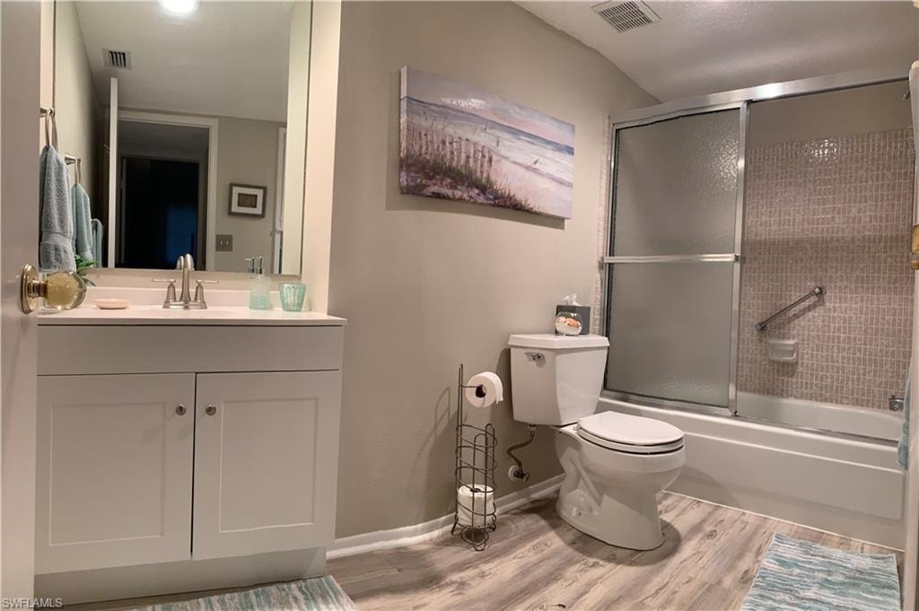 Full bathroom featuring toilet, vanity, bath / shower combo with glass door, and hardwood / wood-style flooring