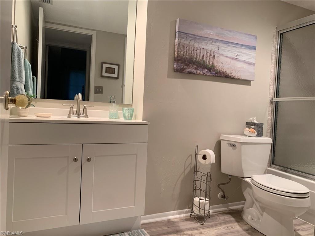 Updated guest bathroom featuring vanity, wood-type flooring, combined bath / shower with glass door, and toilet