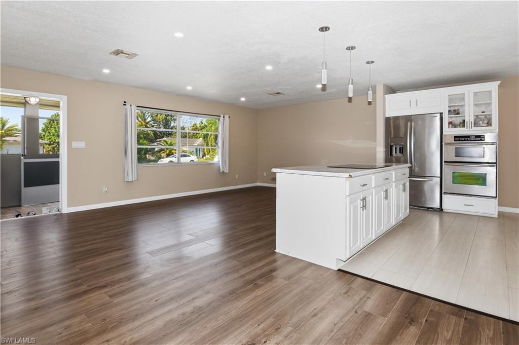 Kitchen featuring open floor plan, white cabinetry, stainless steel appliances, and glass fronted cabinets
