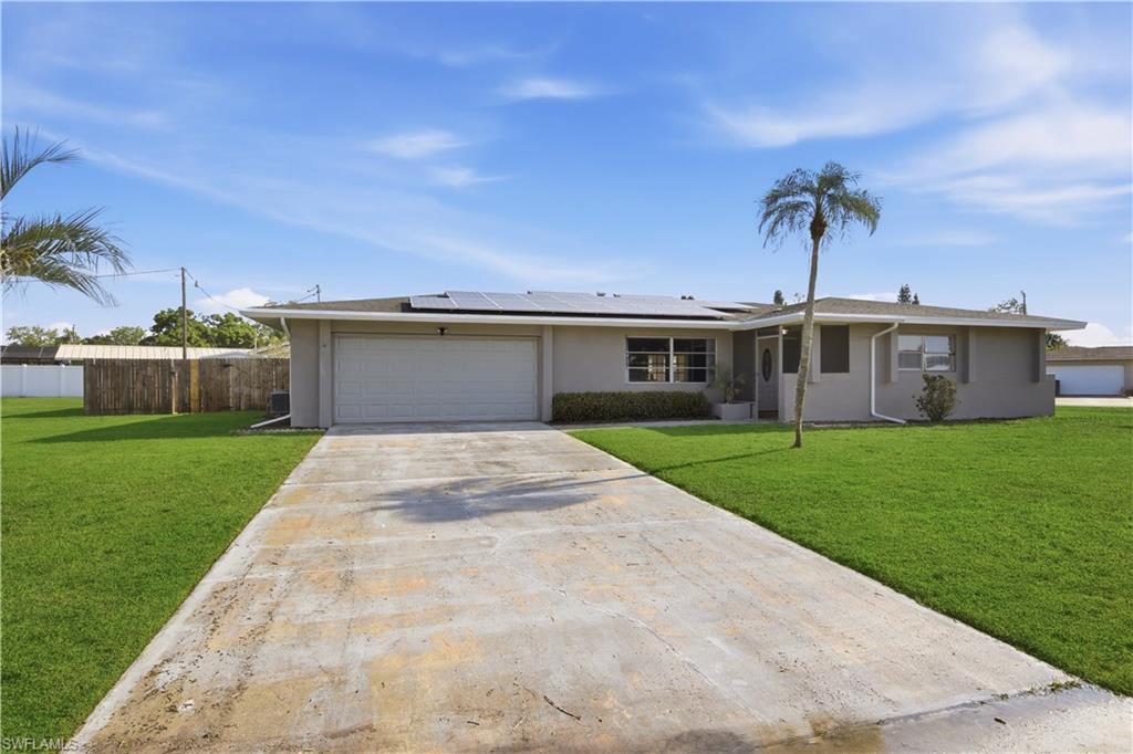 Ranch-style home featuring solar panels, stucco siding, driveway, and an attached garage