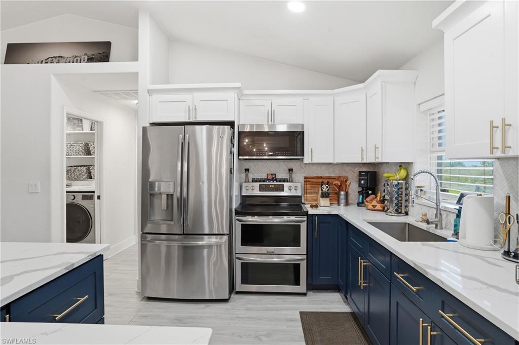 Dual tone kitchen with stainless steel appliances, vaulted ceiling, light stone countertops, two tone cabinetry, and washer / clothes dryer
