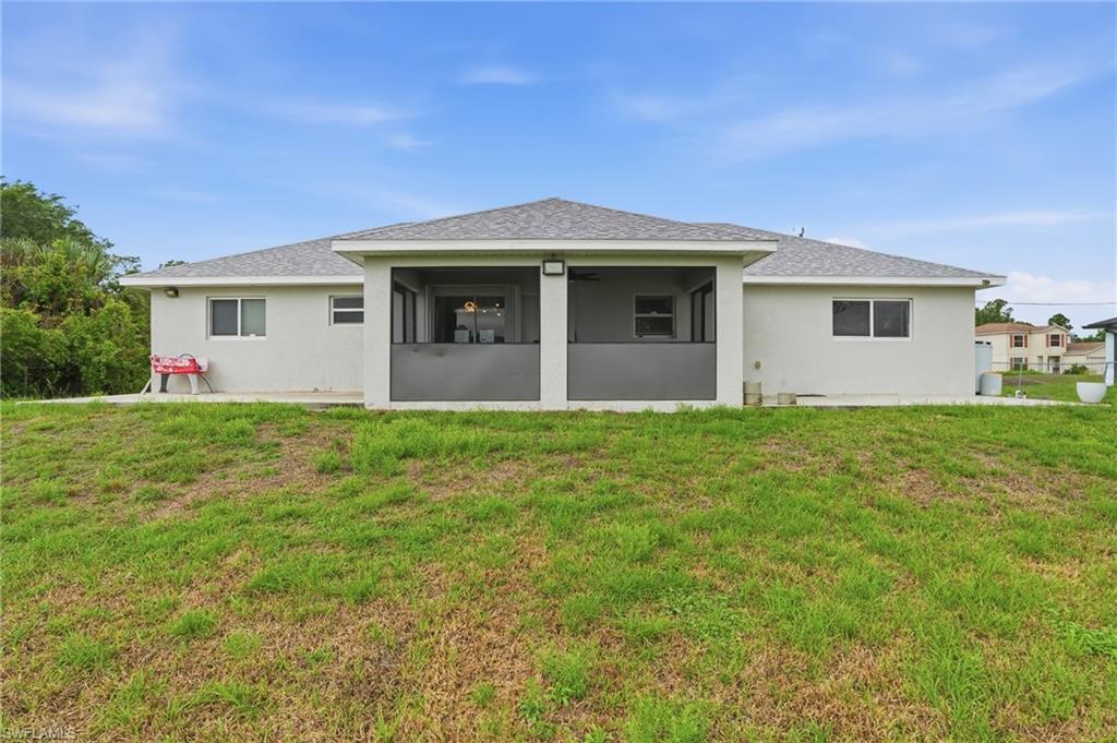 Back of property featuring a yard, stucco siding, a shingled roof, and a sunroom