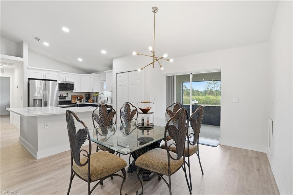 Dining area with suspended lighting, vaulted ceiling, and light wood-style flooring