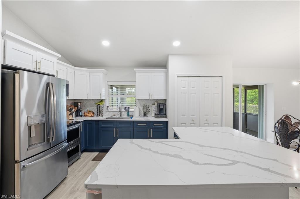 Kitchen featuring two tone cabinetry, stainless steel appliances, light stone counters, a kitchen island, and vaulted ceiling