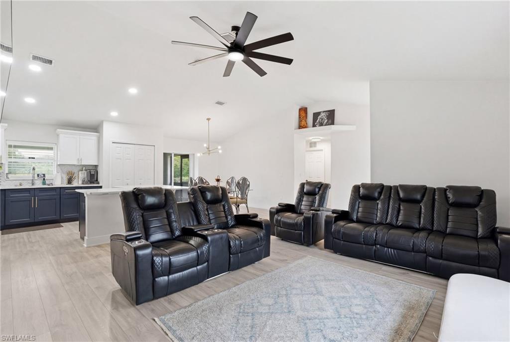 Living area with suspended lighting, a ceiling fan, light wood finished floors, and vaulted ceiling