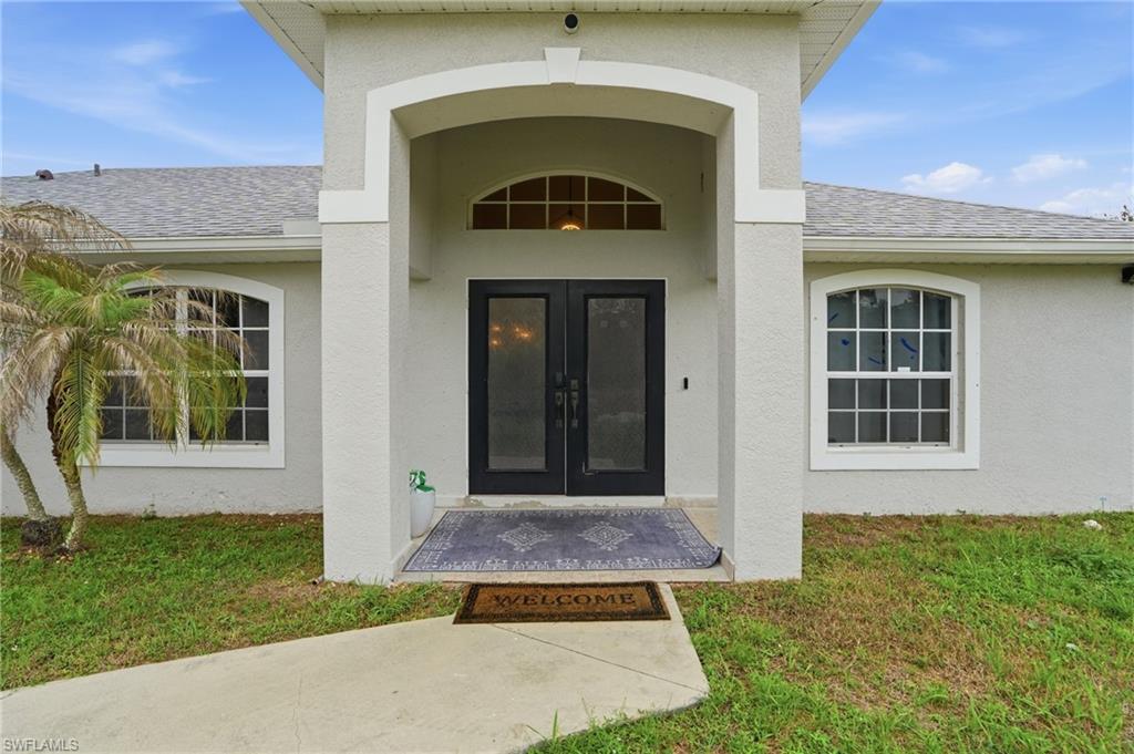 Doorway to property featuring a shingled roof, french doors, stucco siding, and a yard