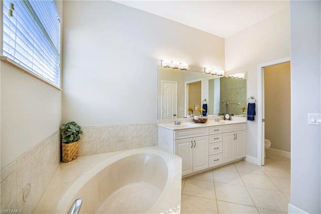Bathroom with double vanity, a bath, and light tile patterned floors
