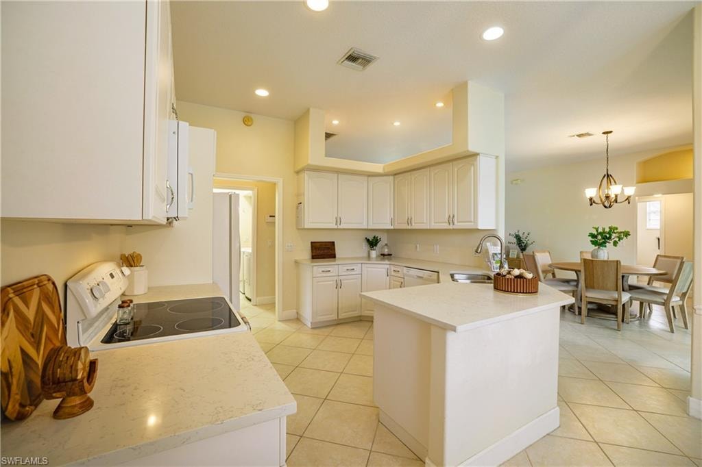 Kitchen featuring white appliances, a peninsula, light tile patterned floors, suspended lighting, and white cabinets