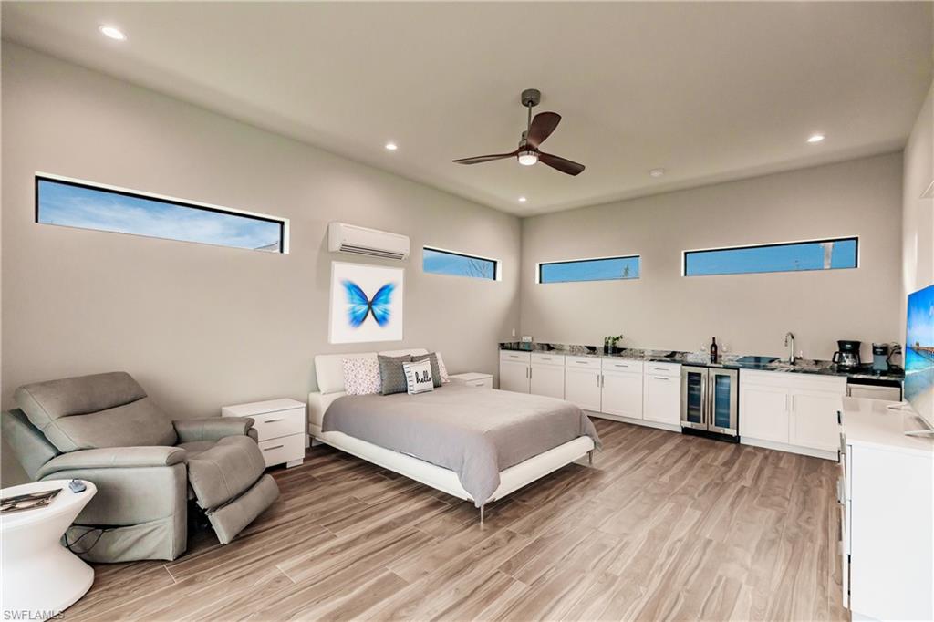 Bedroom featuring light wood-style flooring, bar with sink, multiple windows, and recessed lighting