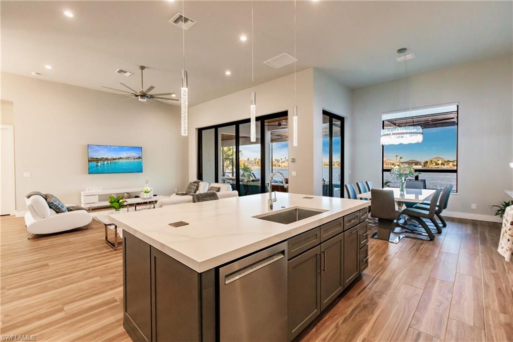 Kitchen featuring stainless steel dishwasher, open floor plan, light wood-style flooring, an island with sink, and a ceiling fan