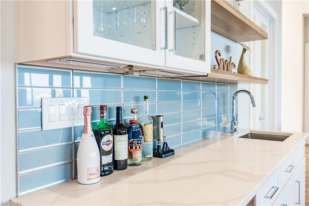 Kitchen featuring backsplash, light stone counters, white cabinetry, and glass insert cabinets