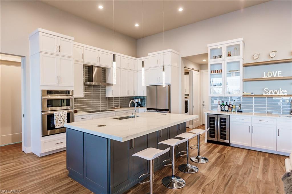 Kitchen featuring appliances with stainless steel finishes, a breakfast bar area, backsplash, wall chimney range hood, and recessed lighting